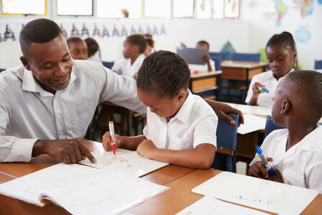 Teacher helping elementary school girl at her desk in class