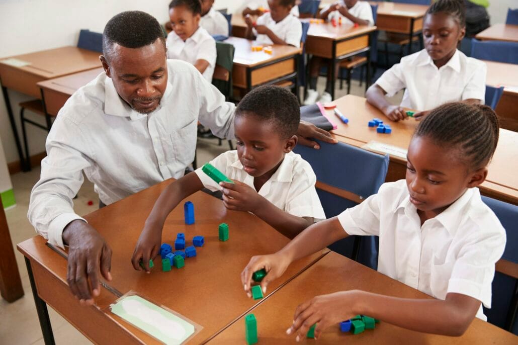 Teacher helping elementary school kids counting with blocks