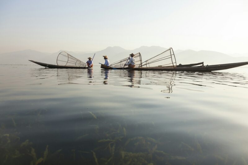 Three fisherman with traditional fishing nets on boats on a lake.
