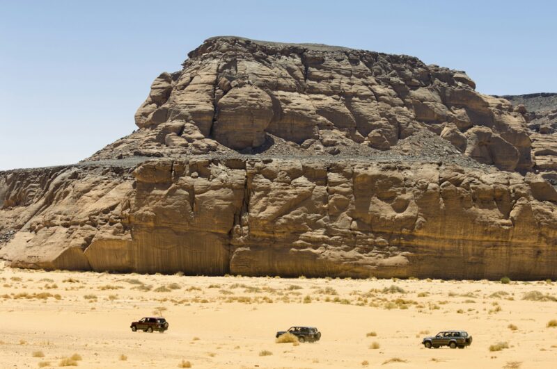 Three Vehicles driving past Wadi Teshuinat, Akakus, Sahara desert, Fezzan, Libya