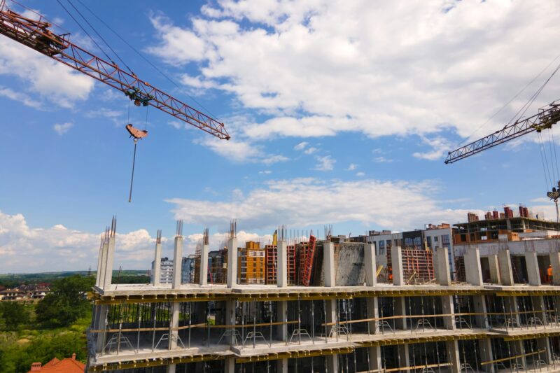 Tower crane at high concrete residential building under construction. Real estate development