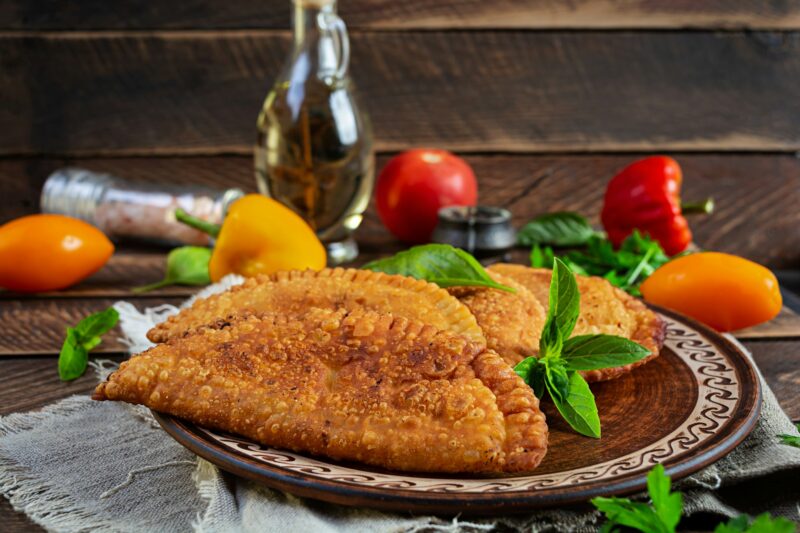 Traditional Crimean Tatar cuisine, chebureki with chicken meat. Fried empanadas on wooden background