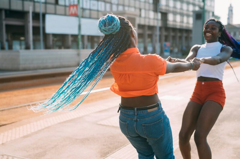 Two black young sisters outdoors city spinning around holding hands laughing