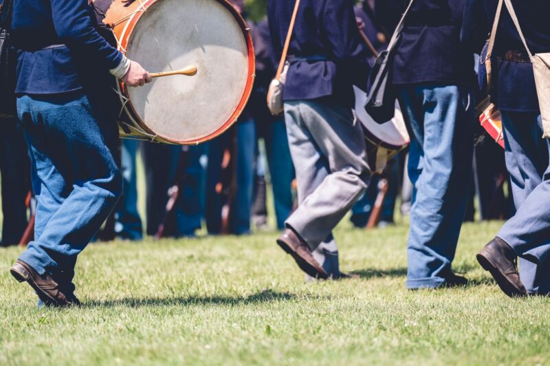 Veterans marching and playing musical instruments in a field reenacting the American Civil War.