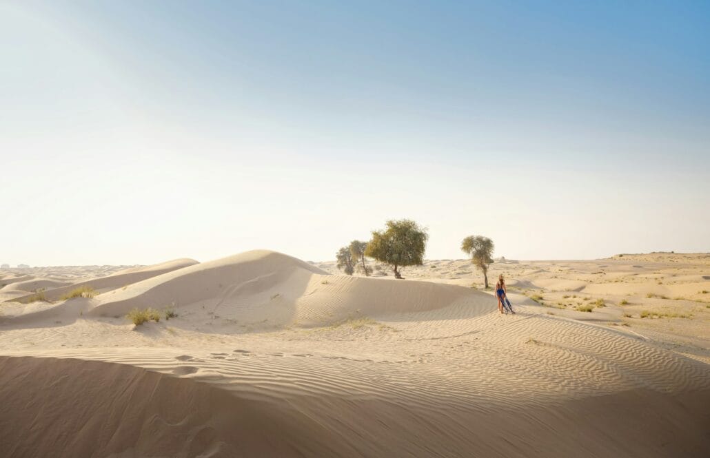 Woman in sands dunes of desert at sunset