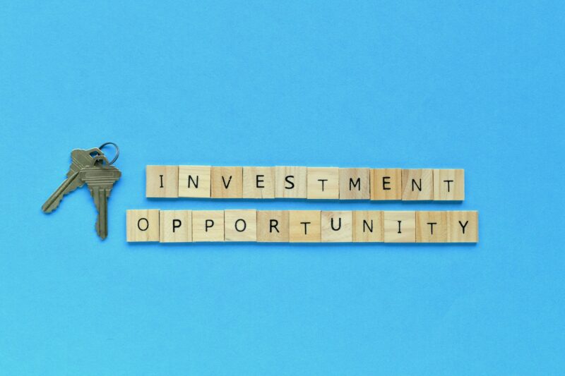 Words Investment Opportunity wood letter tiles with a set of house keys next to it. Real estate
