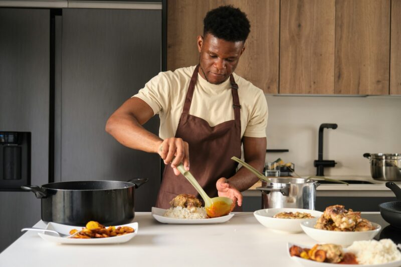 Young african man serving tomato sauce on fried chicken and rice on a plate.
