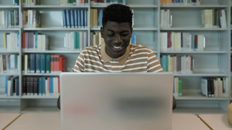 Young African student using laptop in library - School education concept