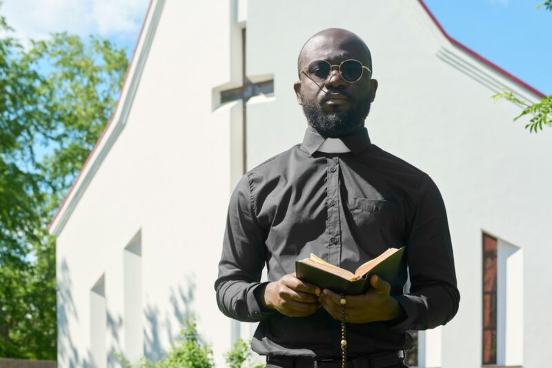 Young black man in shirt with clerical collar standing with open Bible