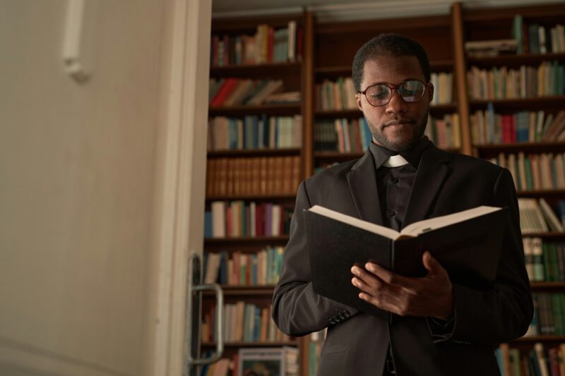 Young Black Priest Reading Bible in Office