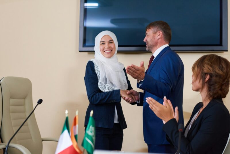 Young confident businessman shaking hand of successful female speaker