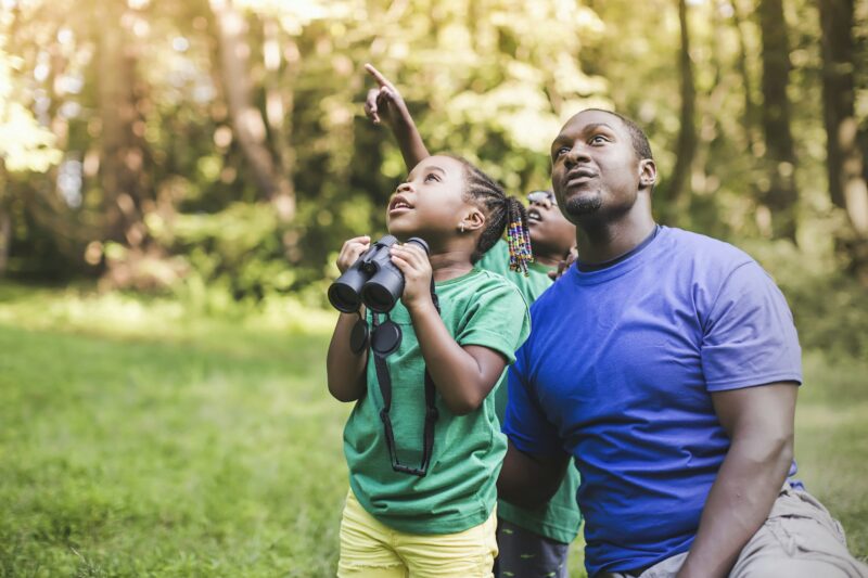 Young father with son and daughter bird watching in eco forest camp