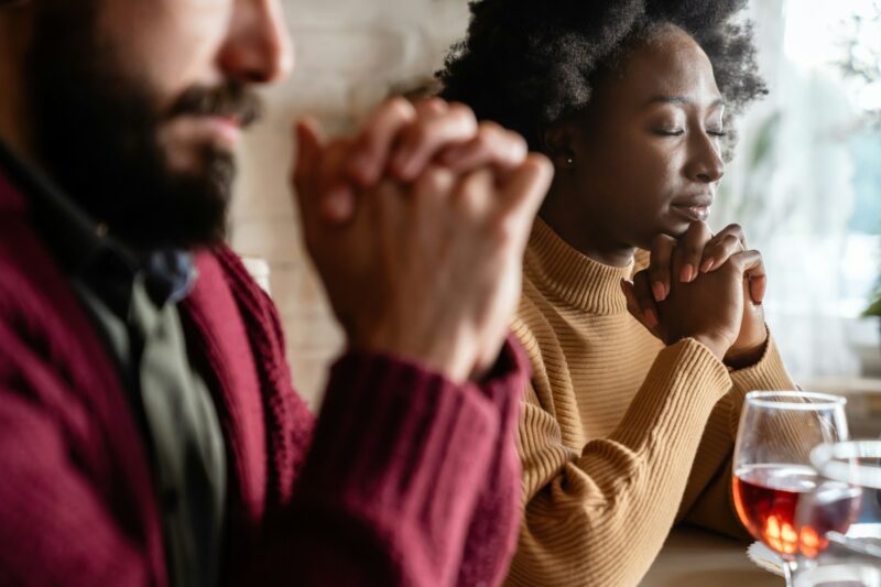 Young multiethnic couple praying to Lord to bless their food and day