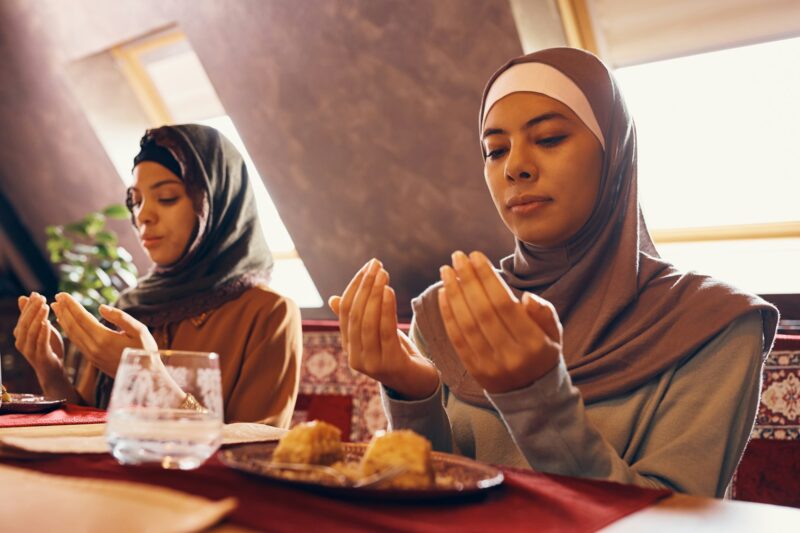 Young Muslim women praying while having dessert at home.