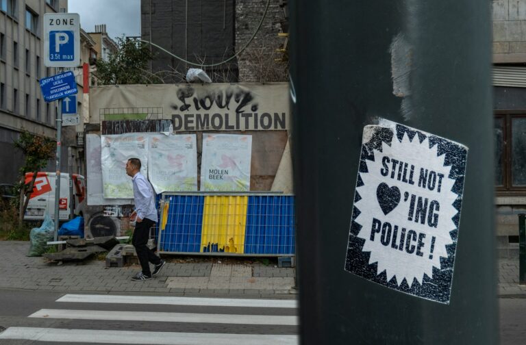 still not loving' police sticker stamped on pole overlooking person standing beside pedestrian lane at daytime