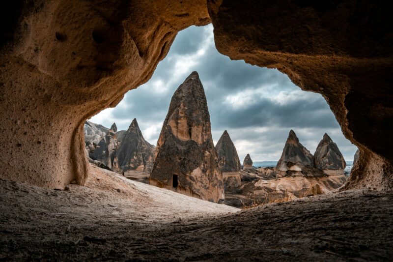 a cave filled with brown rock formations near mountains and clouds