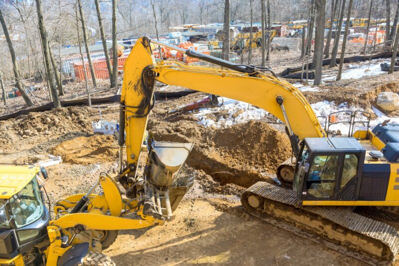 A large excavator is digging on an industrial site for development of infrastructure