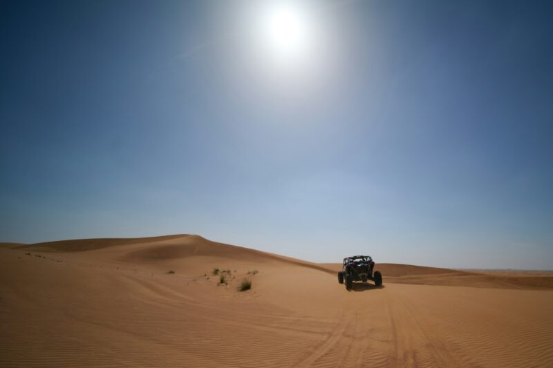 a person riding in a jeep through a sand dunes under a bright sun