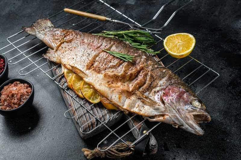 BBQ roasted sea trout, grilled fish on a grill with rosemary. Black background. Top view