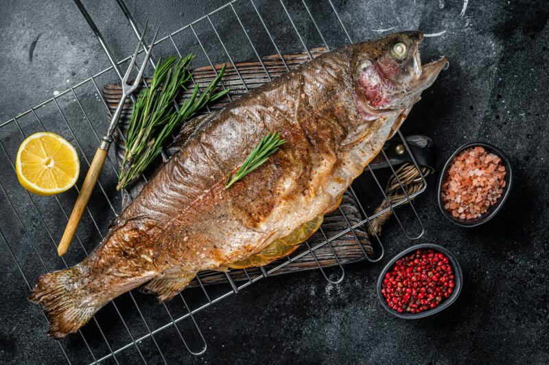 BBQ roasted sea trout, grilled fish on a grill with rosemary. Black background. Top view