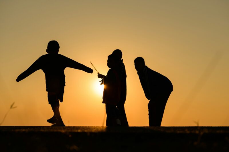 Child silhouette playing fun with many friends and playing against the sunset.