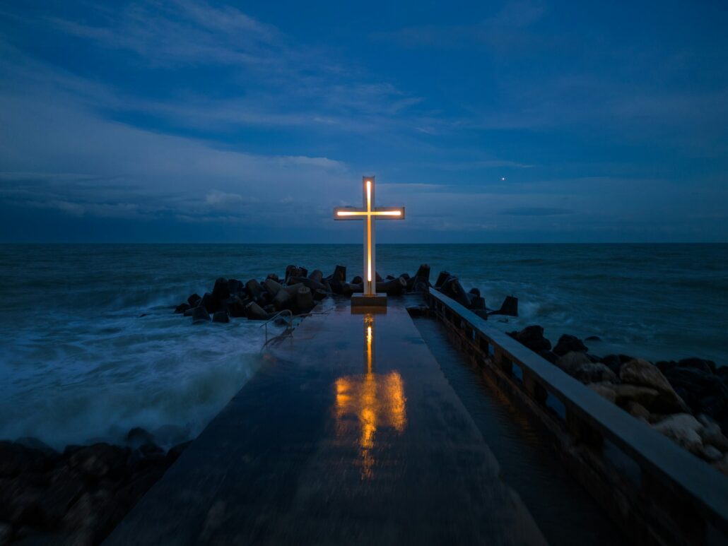 christian cross standing on pier in the sea or ocean with dramatic sky at night