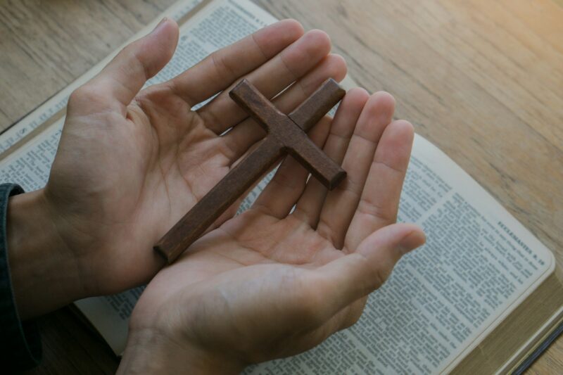 Christian man holding jesus cross.Hands folded in prayer on a Holy Bible on wooden table.