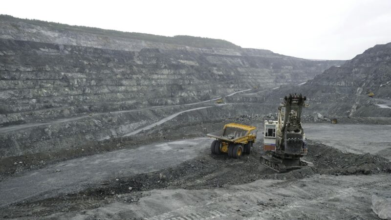 Excavator fills dump truck with earth in open pit. Heavy machinery works in mining industry in open