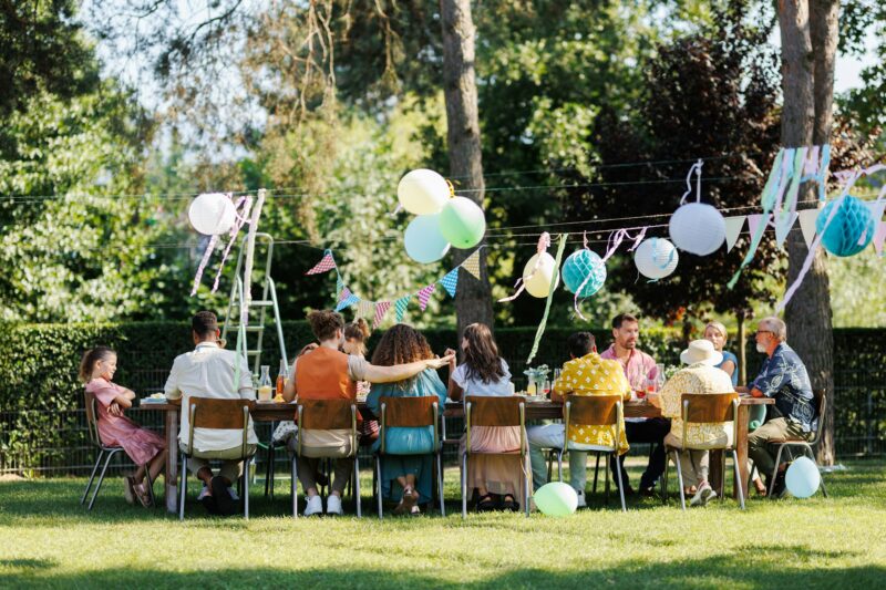 Family and friends sitting at the party table during a summer garden party outdoors. Rear view of