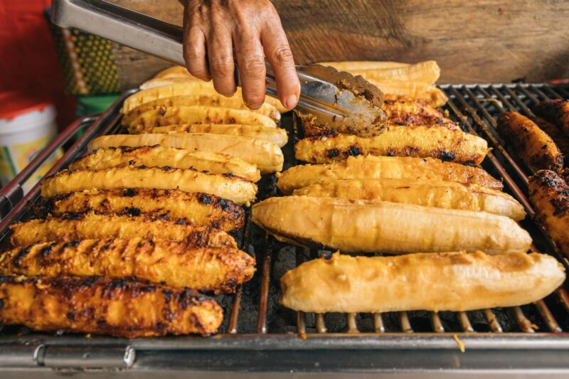 Hands of an unrecognizable person, grilling plantains at a street market stall