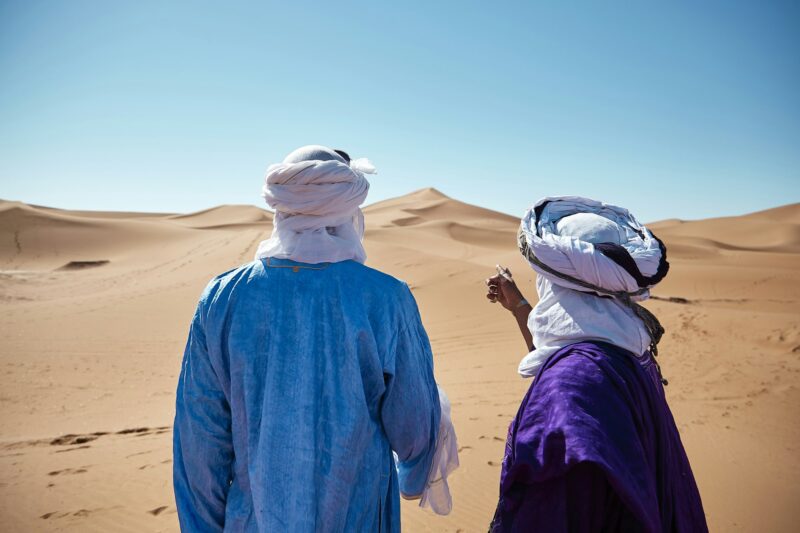 Horizontal shot of two friends standing in front of Chigaga dunes in the Moroccan desert