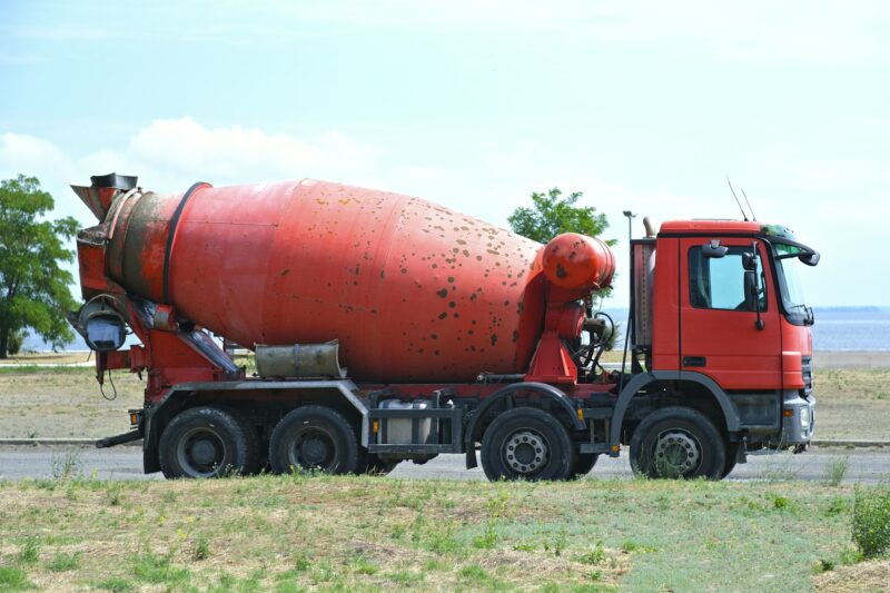 Large red old rusty concrete mixer stands on the street. Clear sunny day. Repair, industry.