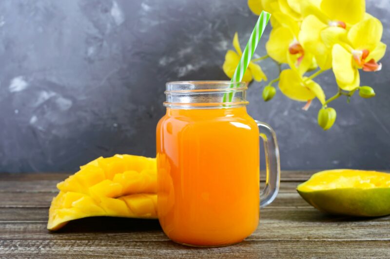 Mango smoothie in a glass jar and fresh mango