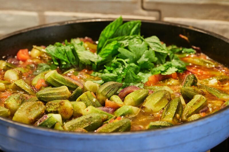 Okra and fried purple onions are pan-fried with cilantro and basil on gas stove