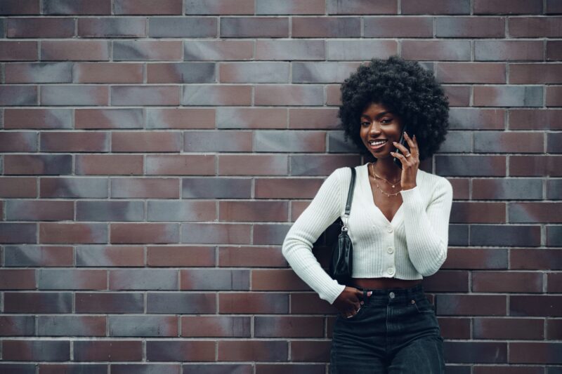 Portrait of happy african young woman talking on cellphone in city