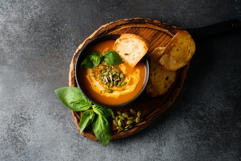 Pumpkin soup with bread, seeds and basil leaf on dark background