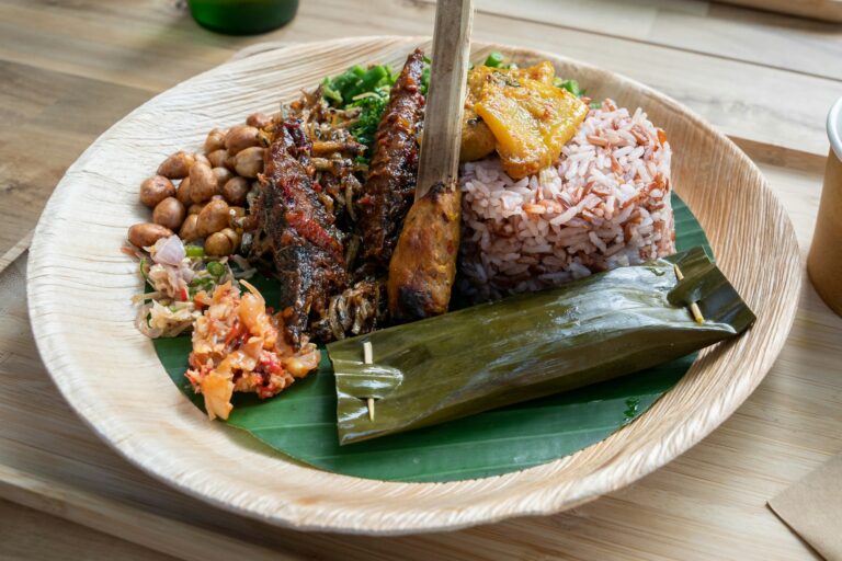 Side view of a plate of Balinese food with fish, sate, soup, rice, sambal, greens on bamboo plate