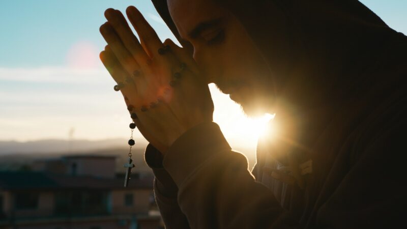 Silhouette of praying man with christian crucifix