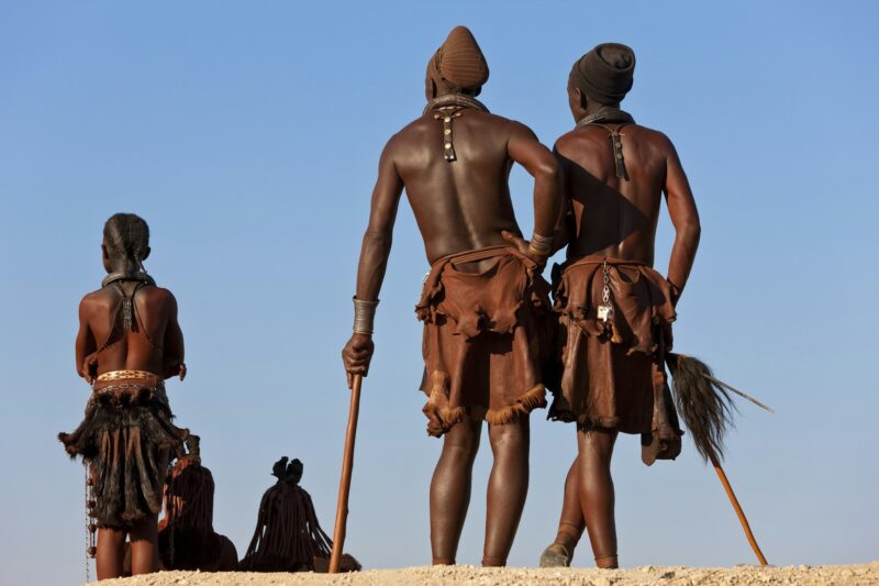 Small group of Himba men wearing traditional clothing standing in a desert.