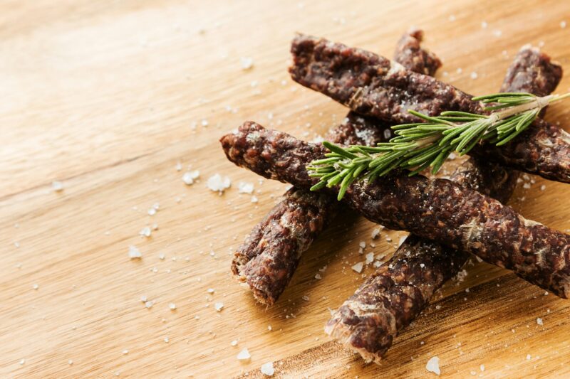 Sticks of traditional South African droewors with a rosemary seasoning on a wooden surface