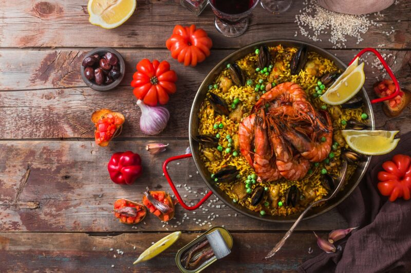 Top view of paella with prawns, mussels and lemon, wooden background