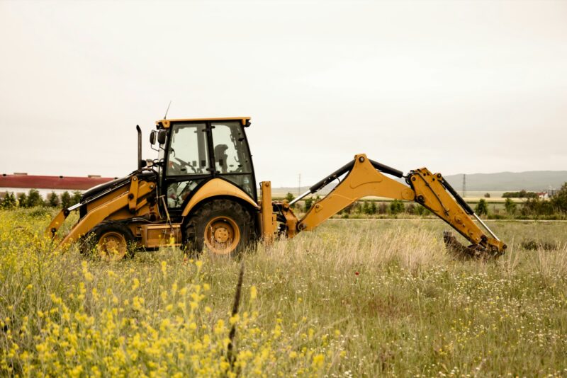 Tractor excavator against the background of spring flowers in the field. Preparing fields for sowing